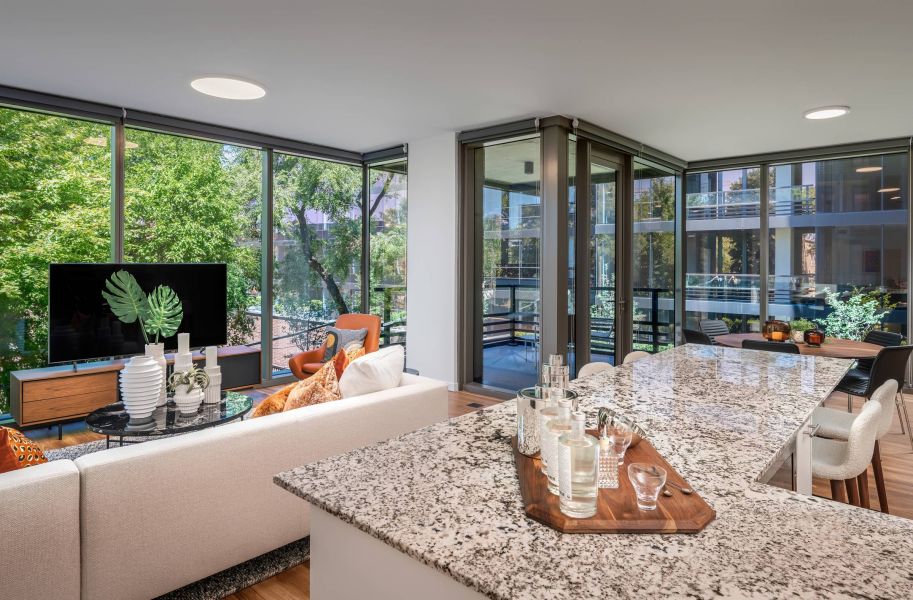 Optima Lakeview® Apartments in Chicago, IL Modern living room and kitchen with large windows, granite island, and views of trees and balconies outside.