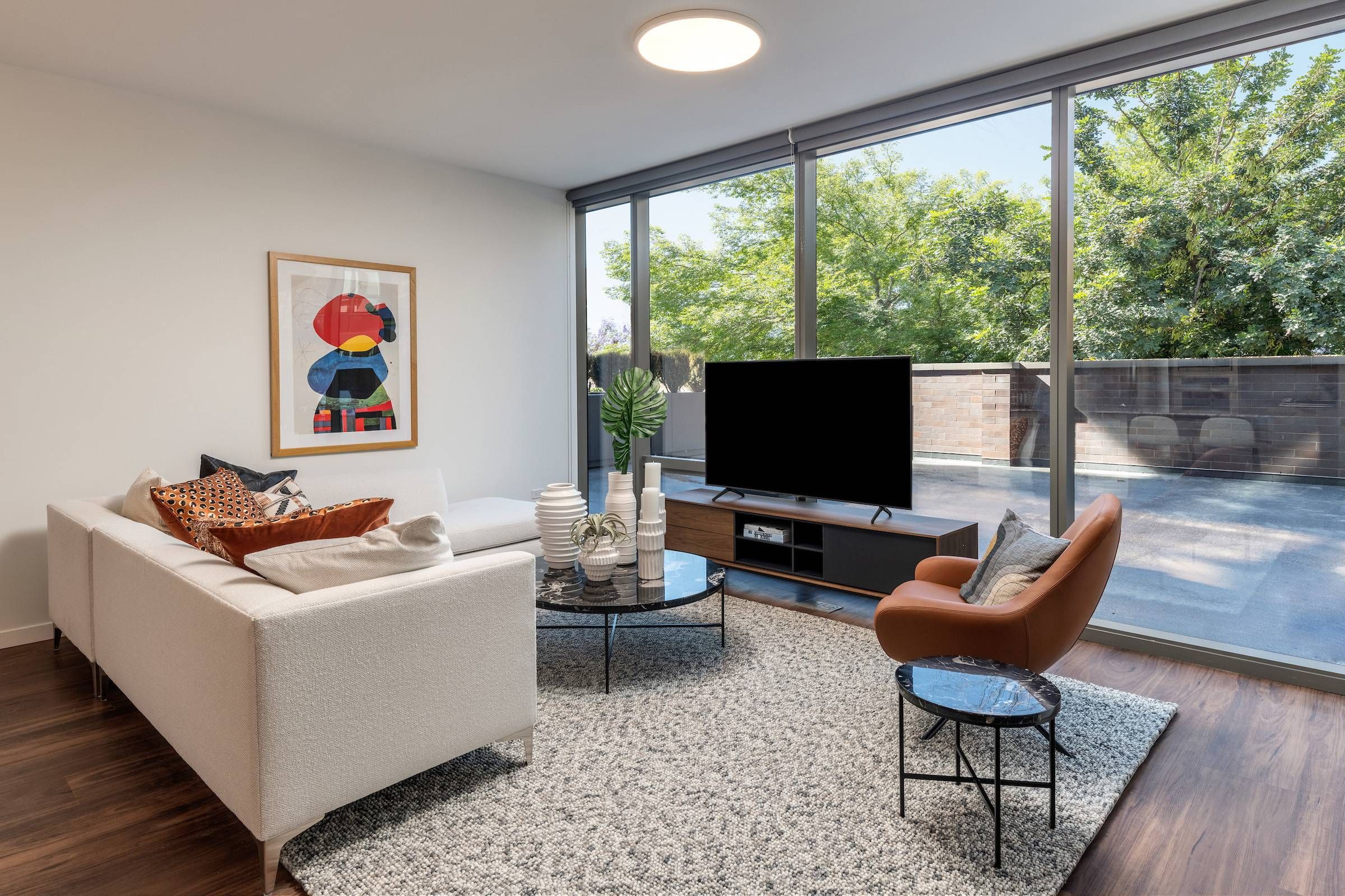 Optima Lakeview® Apartments in Chicago, IL Modern living room with large windows, white sofa, orange chair, TV, and abstract art on the wall.