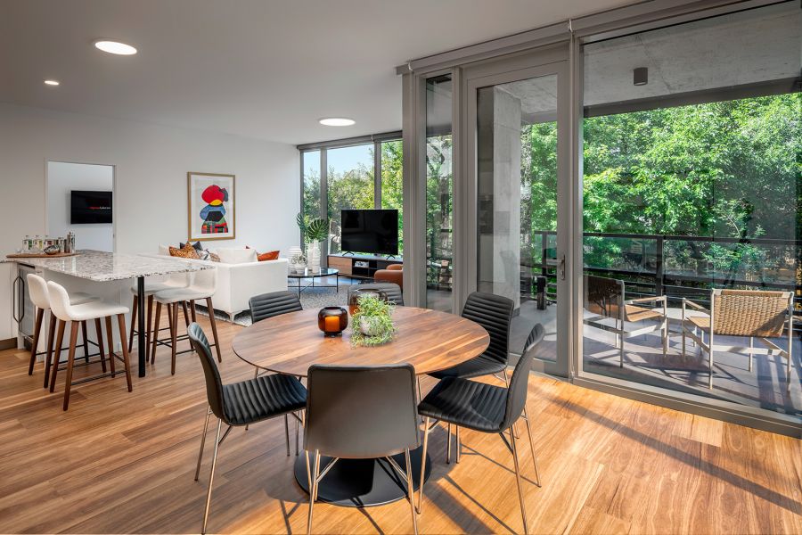 Optima Lakeview® Apartments in Chicago, IL Modern open-plan living and dining area with large windows and balcony overlooking green trees.