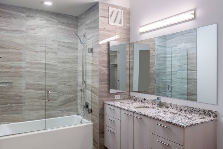 Optima Lakeview® Apartments in Chicago, IL Modern bathroom with glass shower, granite countertop, large mirror, and light wood cabinets.