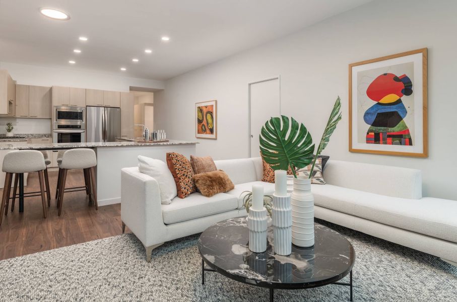 Optima Lakeview® Apartments in Chicago, IL Modern living room with white sofas, abstract art, plants, and a marble coffee table near an open kitchen.
