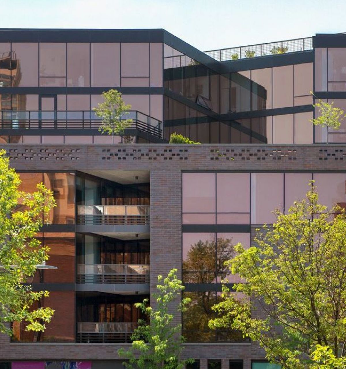 Optima Lakeview® Apartments in Chicago, IL Modern glass building with trees in front, reflecting the blue sky and nearby structures.