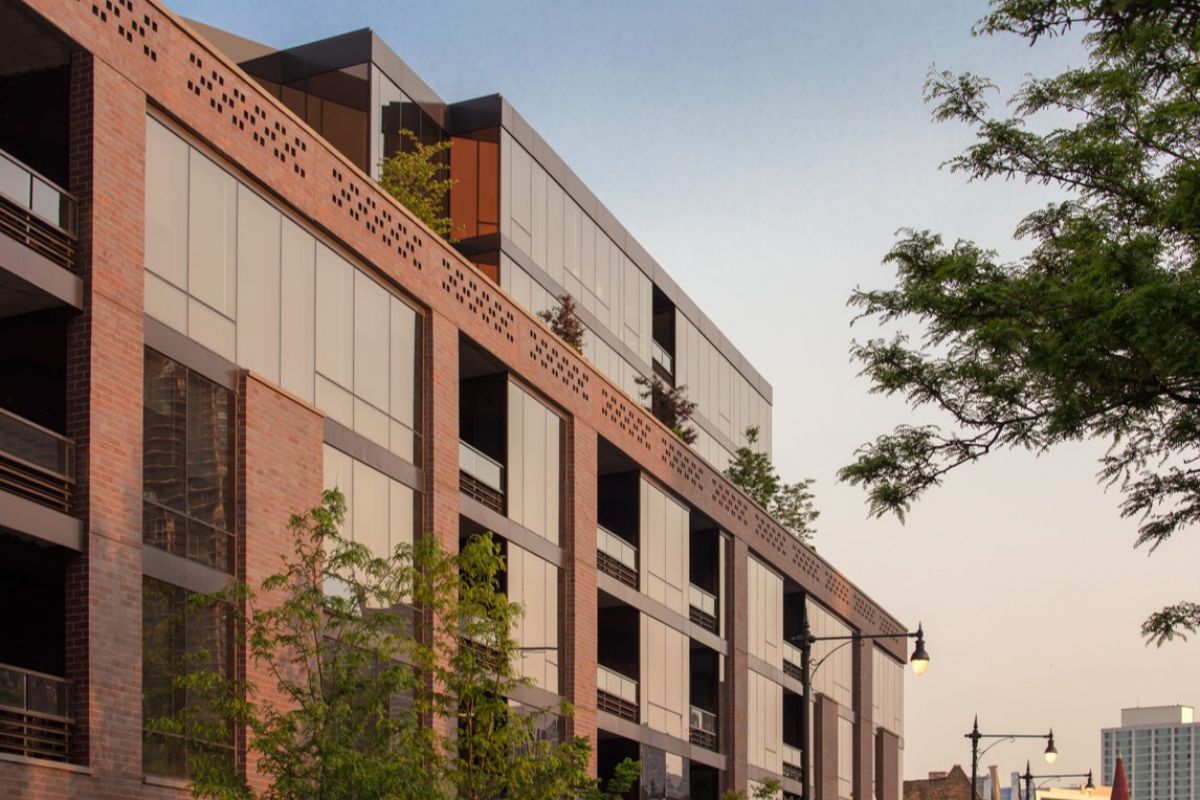 Optima Lakeview® Apartments in Chicago, IL Modern apartment building with large windows, brick facade, and trees in the foreground under a clear sky.