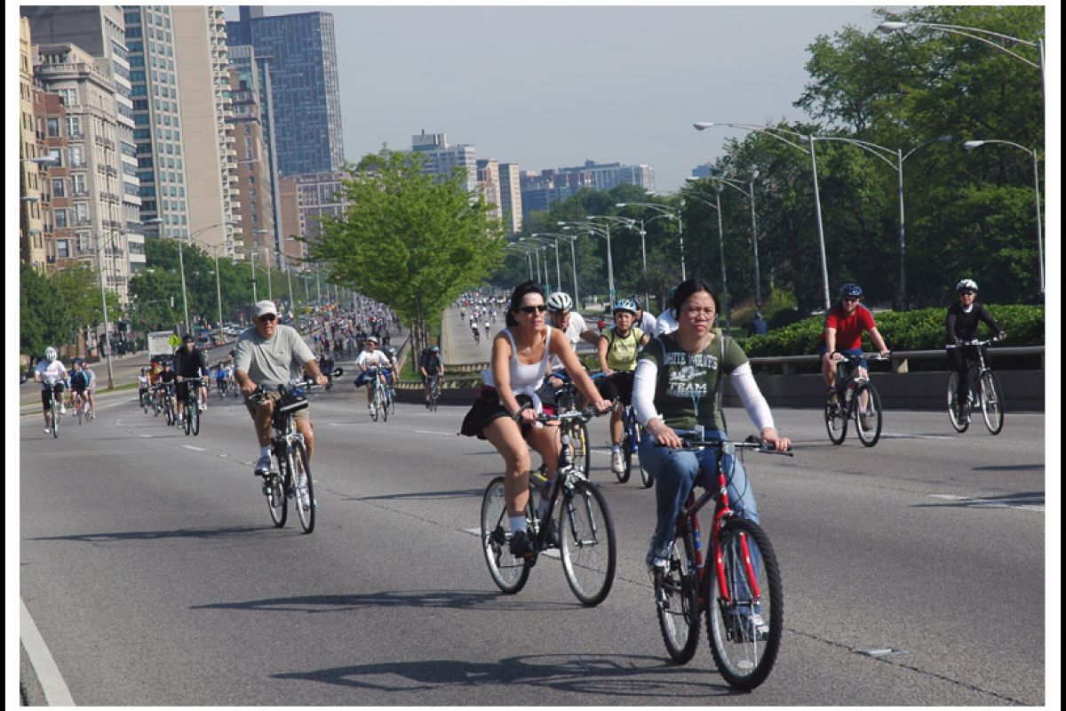 Optima Lakeview® Apartments in Chicago, IL A large group of people riding bicycles on a city street during Bike the Drive 2024, surrounded by tall buildings and trees in Chicago.