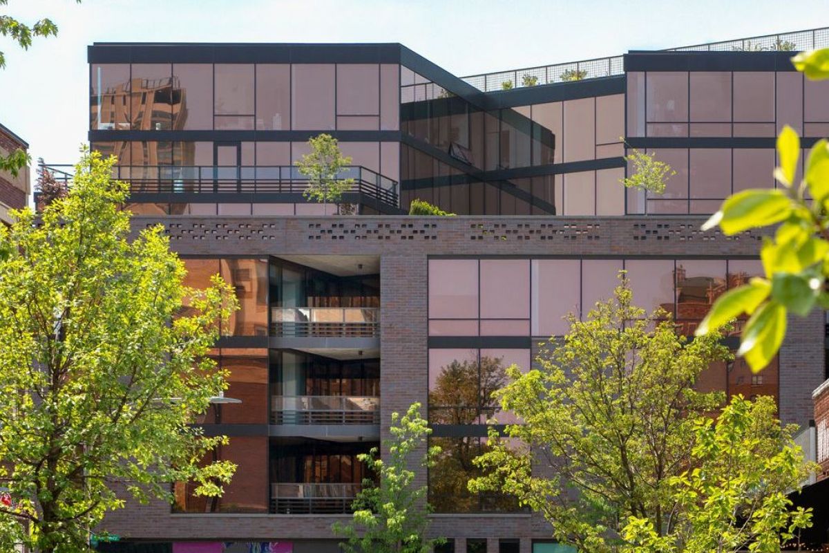 Optima Lakeview® Apartments in Chicago, IL Modern glass building with trees in front, reflecting the blue sky and nearby structures.