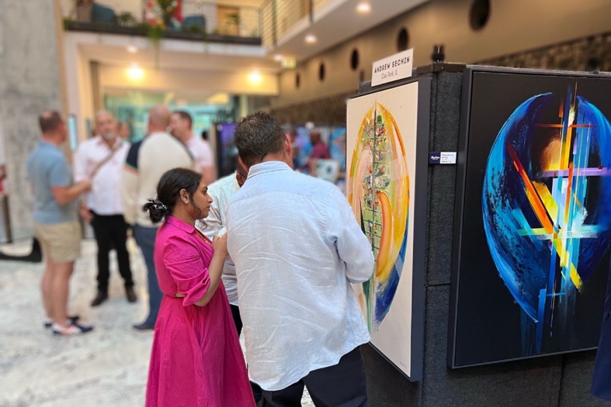 Optima Lakeview® Apartments in Chicago, IL People view colorful abstract art at an Optima Communities gallery celebration, while others mingle and enjoy the lively event in the background.