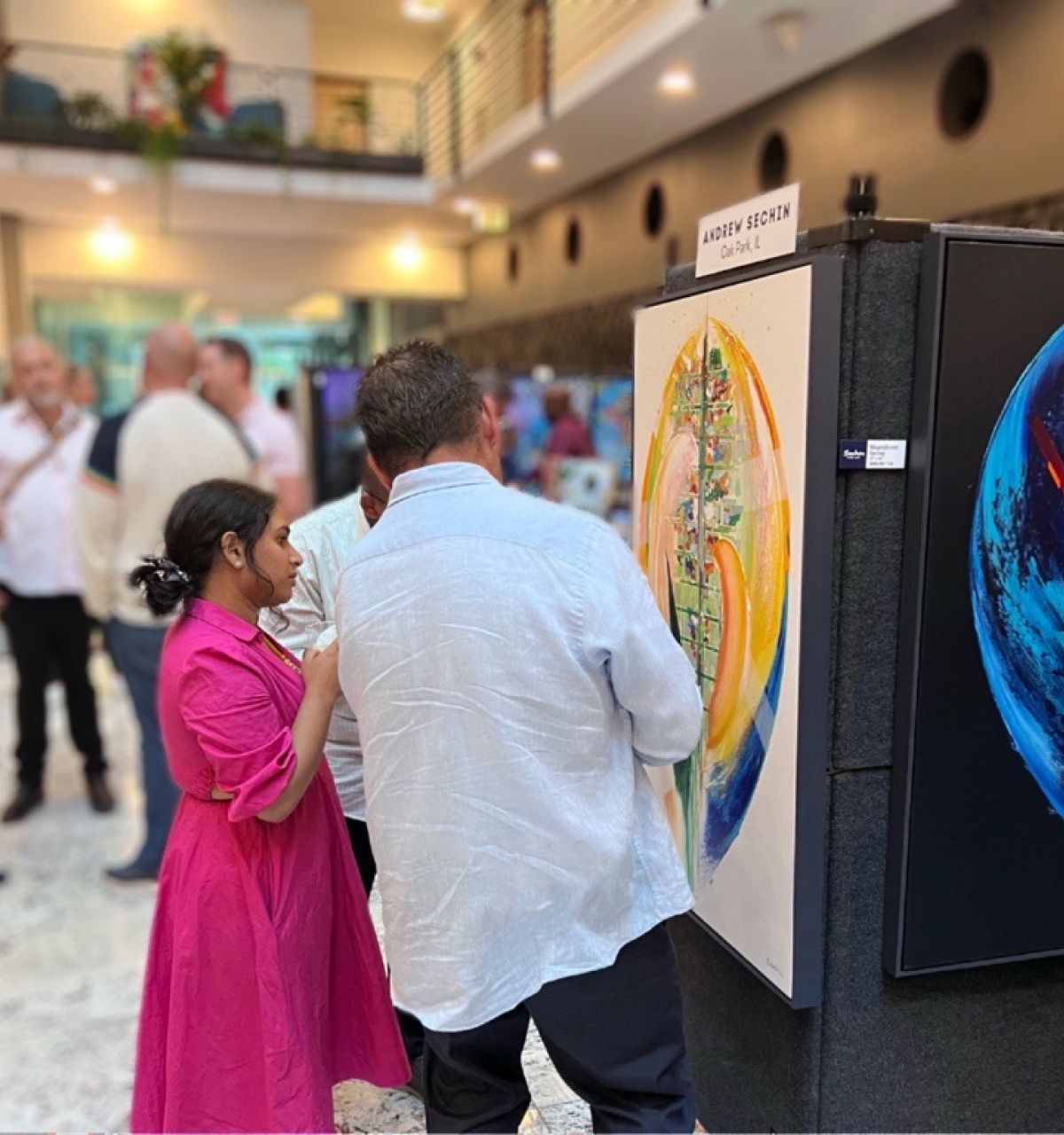 Optima Lakeview® Apartments in Chicago, IL People view colorful abstract art at an Optima Communities gallery celebration, while others mingle and enjoy the lively event in the background.