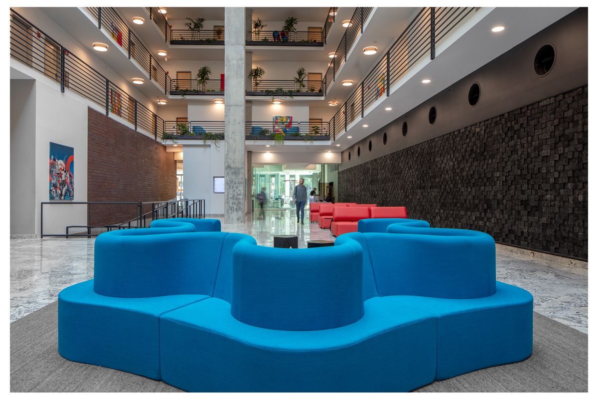 Optima Lakeview® Apartments in Chicago, IL Modern lobby with blue and red Cloverleaf Sofa by Verner Panton, marble floor, and open balconies adorned with lush plants.