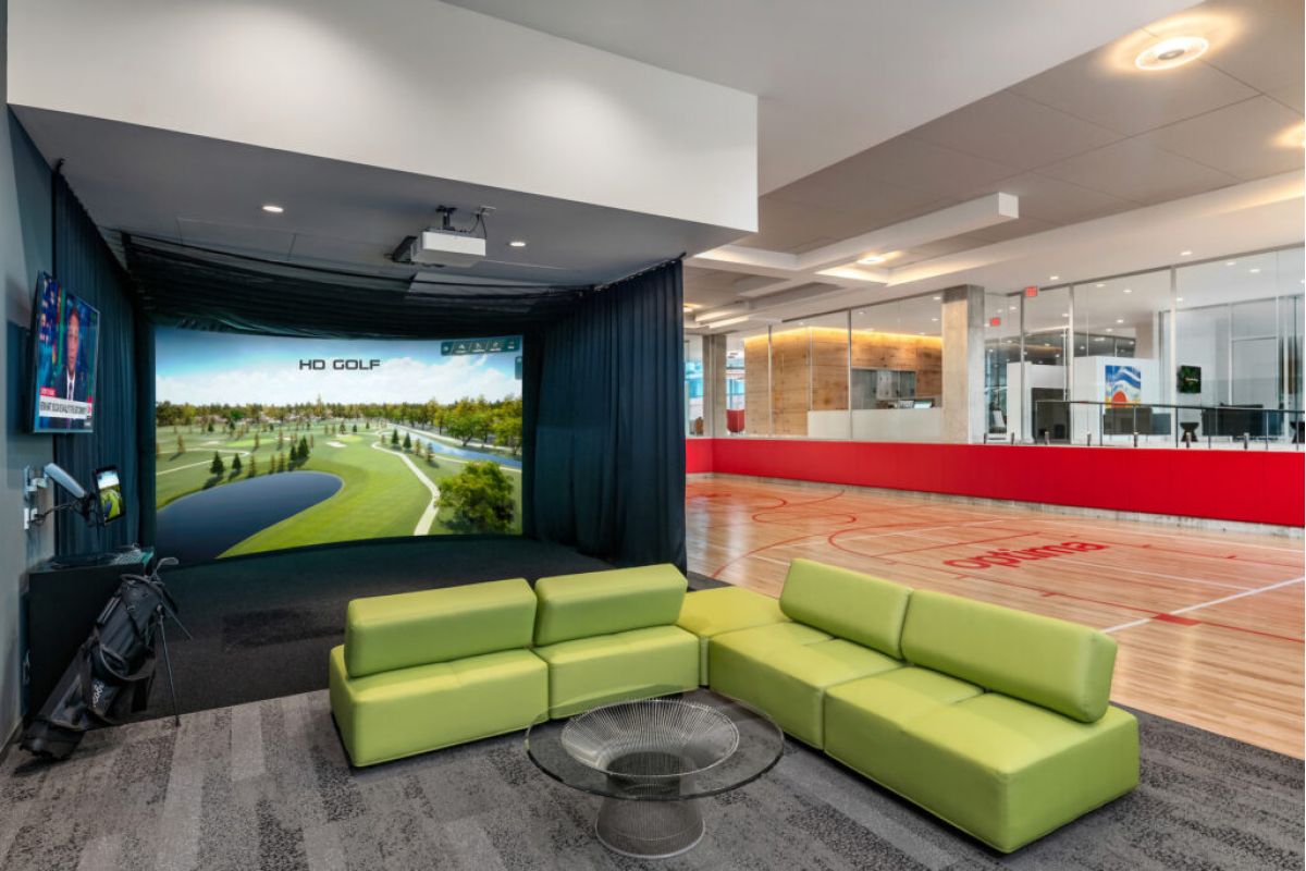 Optima Lakeview® Apartments in Chicago, IL Modern lounge with green sofas, glass table, and golf simulator—luxury home vibes in Optima communities with indoor basketball court.