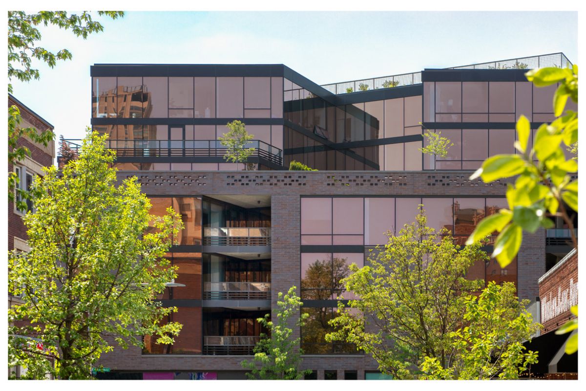 Optima Lakeview® Apartments in Chicago, IL Modern glass architecture with biophilic design, featuring trees in front and reflections of Optima Lakeview and blue sky.