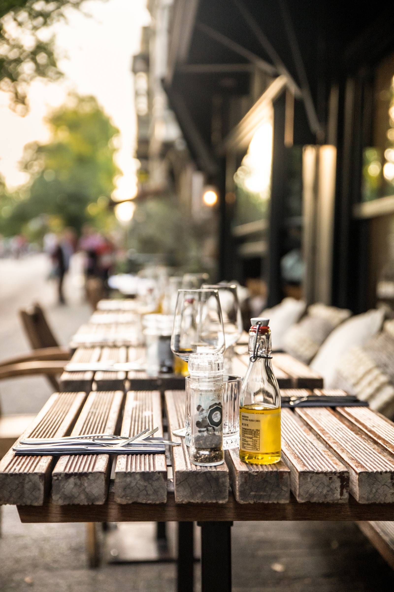 Optima Lakeview® Apartments in Chicago, IL Wooden outdoor restaurant table set with glasses, cutlery, olive oil, and pepper grinder at sunset.