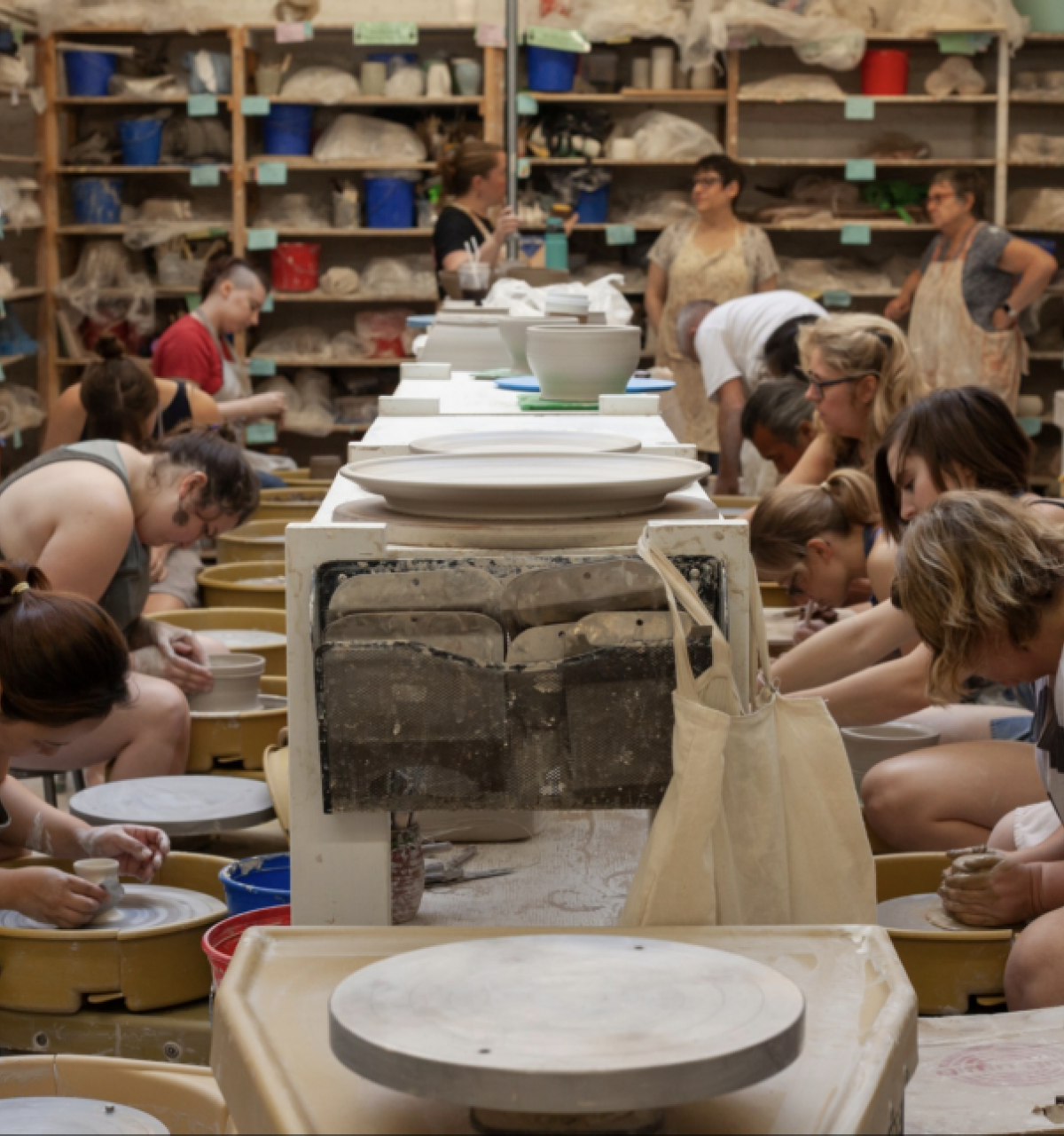 Optima Lakeview® Apartments in Chicago, IL Artists spin clay on pottery wheels at Lillstreet Art Center, surrounded by supplies and bustling with creativity.