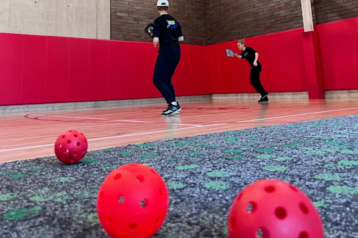 Optima Lakeview® Apartments in Chicago, IL Two people play pickleball in a gym, fostering connection on a carpeted surface with red balls in the foreground.