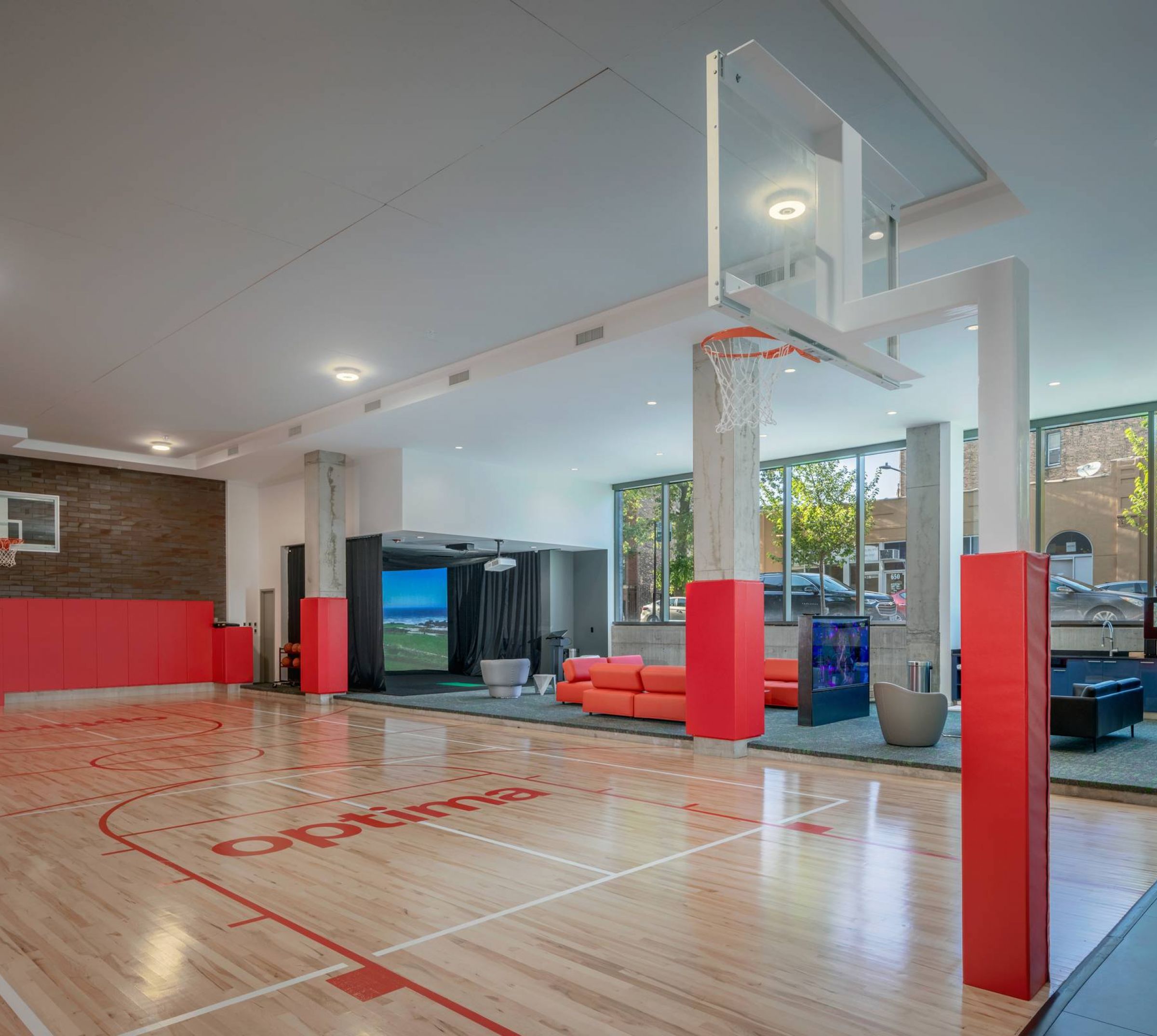 Optima Lakeview® Apartments in Chicago, IL Indoor basketball court with red and white markings, red seating area, and large windows letting in natural light.