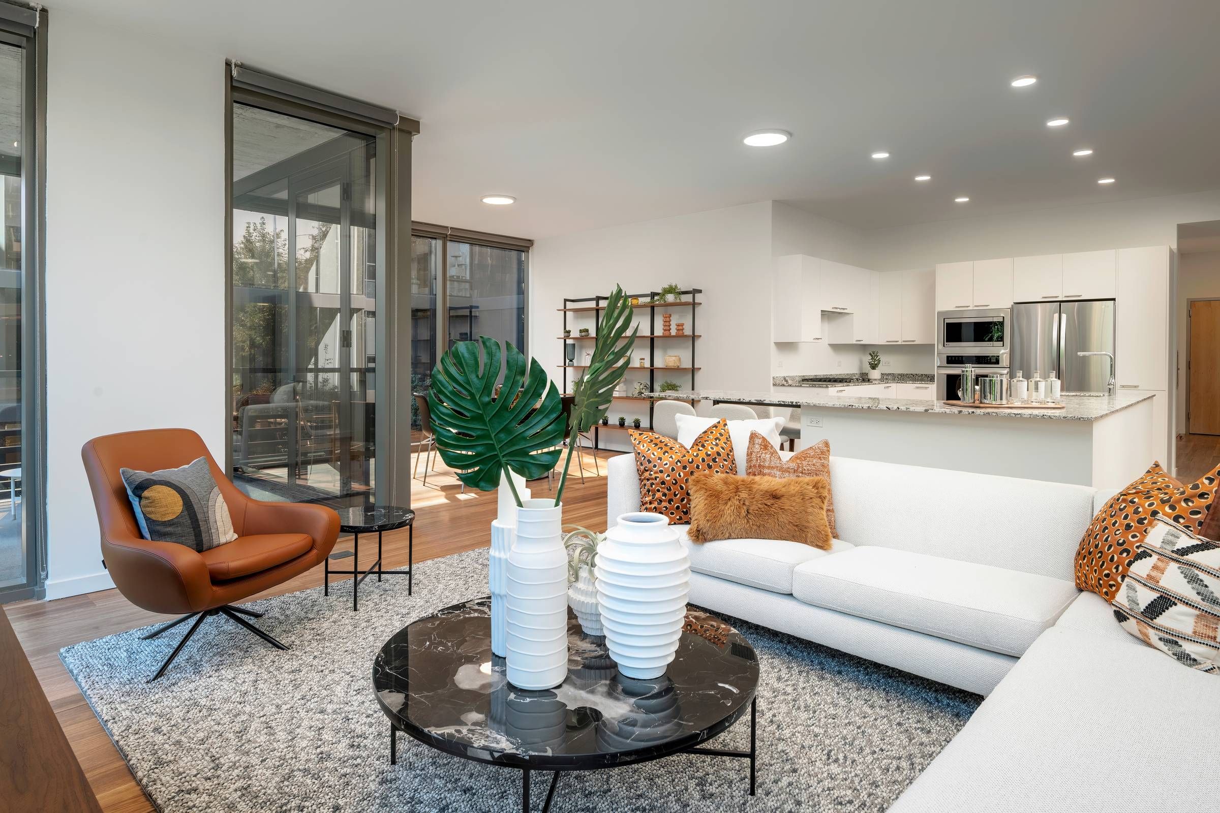 Optima Lakeview® Apartments in Chicago, IL Modern living room with white sofa, brown chair, decorative pillows, and open kitchen in the background.