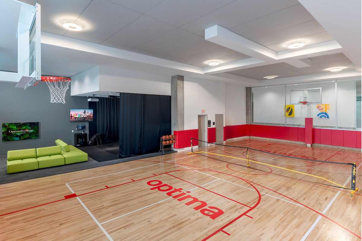 Optima Lakeview® Apartments in Chicago, IL Indoor gym with a basketball court, small tennis net, green couch, and TV in a modern recreational space.
