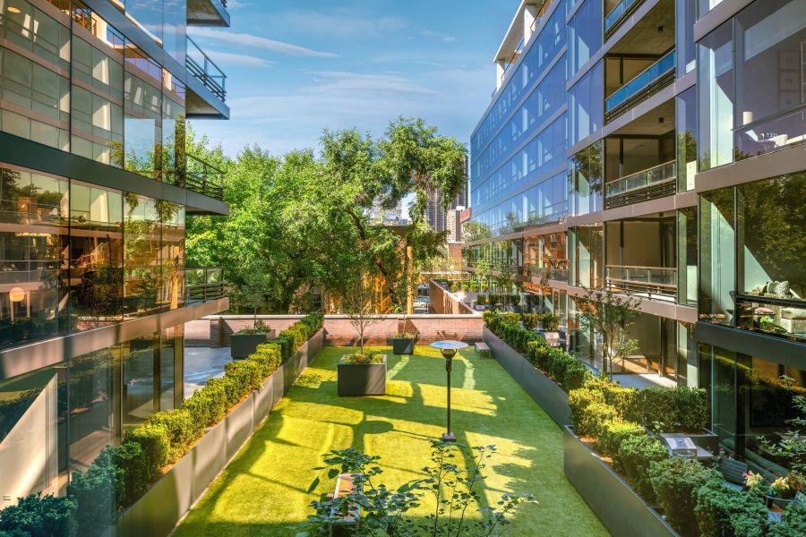 Optima Lakeview® Apartments in Chicago, IL Modern apartment buildings with glass facades overlook a sunny courtyard dog park with trees and green grass.