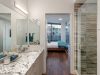 Optima Lakeview® Apartments in Chicago, IL Modern bathroom decor with double sinks and a glass shower, leading to a bedroom with large windows and wood flooring.