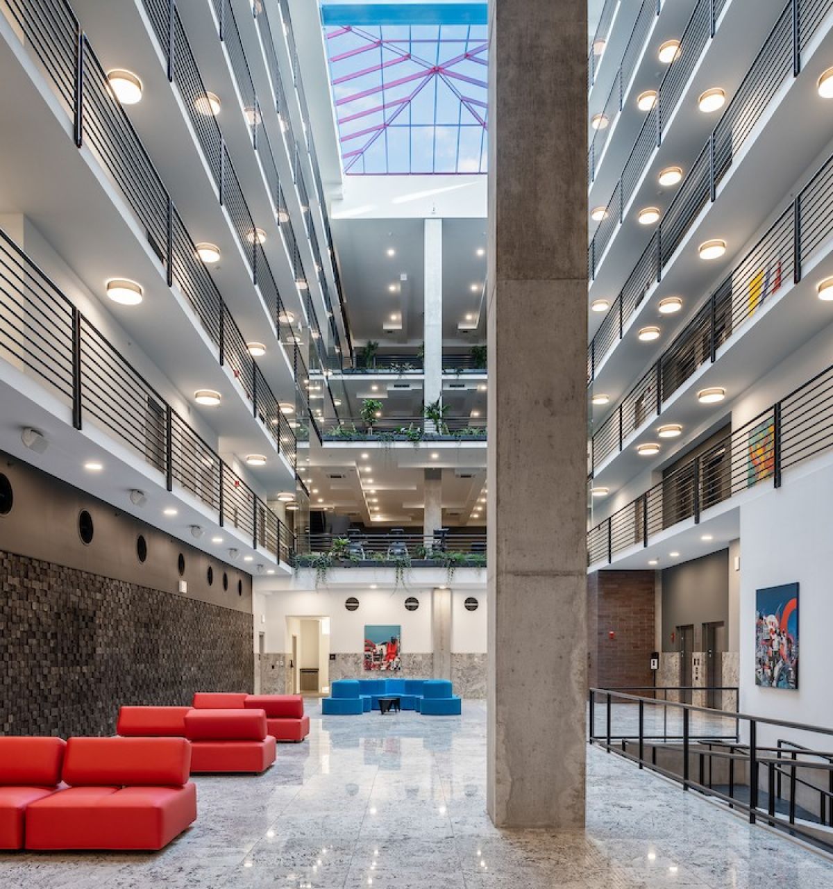 Optima Lakeview® Apartments in Chicago, IL Modern building atrium with red couches, marble floor, balconies, and a skylight ceiling for sunlight health benefits.