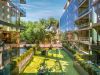 Optima Lakeview® Apartments in Chicago, IL Modern glass buildings with balconies at Optima Lakeview overlook a pet-friendly green courtyard garden with trees and shrubs on a sunny day.