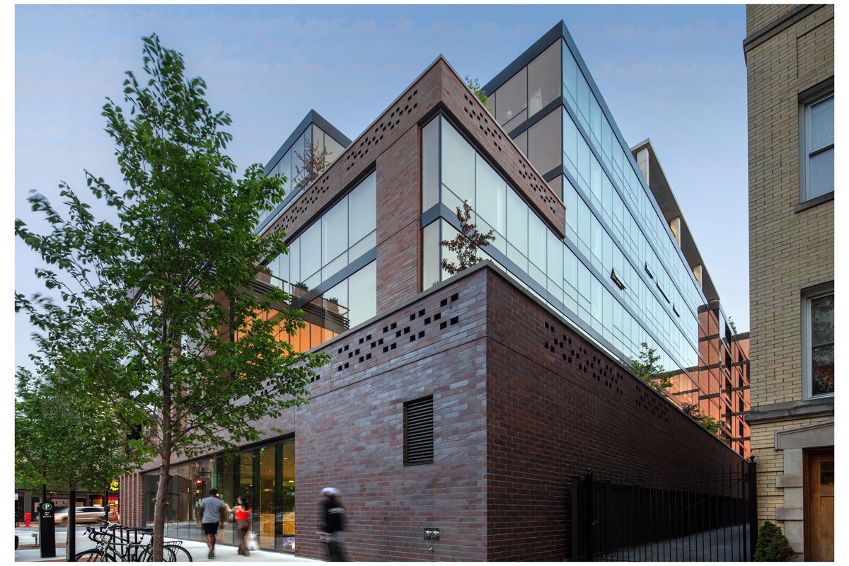 Optima Lakeview® Apartments in Chicago, IL Modern building with glass and brick exterior on a walkable city street, offering new luxury real estate amid trees and bustling sidewalks.