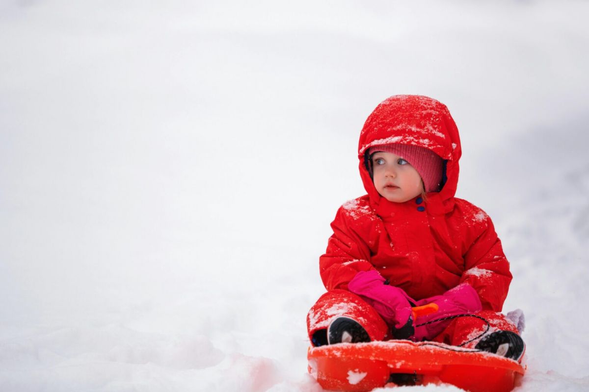 Optima Lakeview® Apartments in Chicago, IL A young child in a red snowsuit sits on a sled, ready for winter fun on the snowy sledding hills.