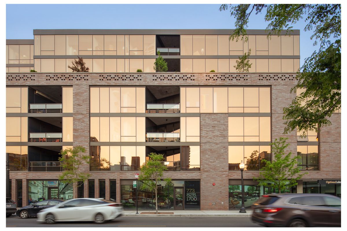 Optima Lakeview® Apartments in Chicago, IL Modern building with large glass windows and brick exterior, cars driving past, and reflections that show our optimized service in the city.