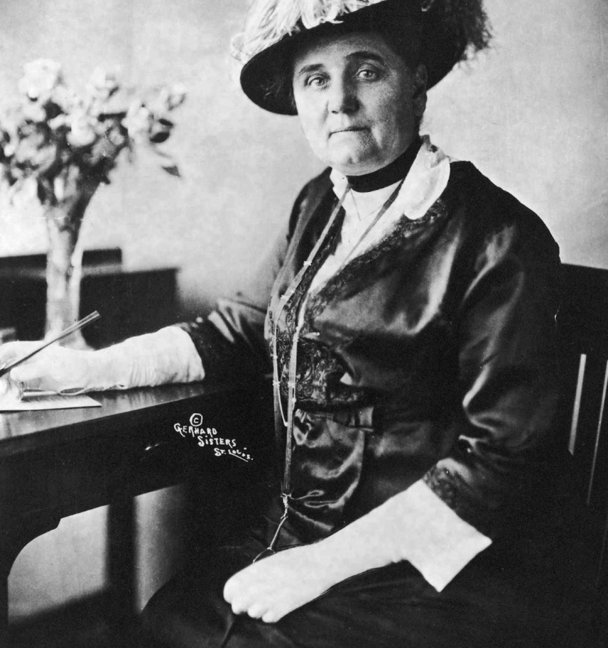 Optima Lakeview® Apartments in Chicago, IL A woman in early 20th-century attire, evoking Jane Addams, sits at a desk with a feathered hat, pen in hand—one of the great Chicago writers.