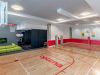 Optima Lakeview® Apartments in Chicago, IL Indoor gym with a basketball court, small tennis net, green couch, and TV in a modern recreational space.