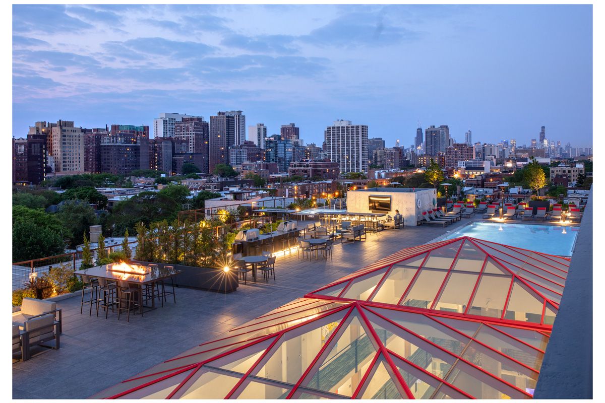 Optima Lakeview® Apartments in Chicago, IL Rooftop patio with seating, fire pits, pool, and city skyline view at sunset—exclusively for Optima Residents to rent and enjoy.