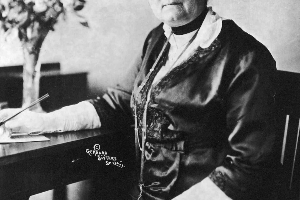 Optima Lakeview® Apartments in Chicago, IL A woman in early 20th-century attire, evoking Jane Addams, sits at a desk with a feathered hat, pen in hand—one of the great Chicago writers.
