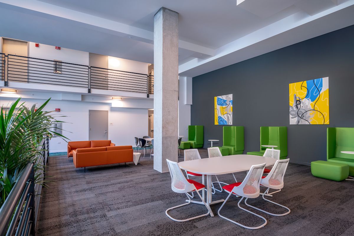 Optima Lakeview® Apartments in Chicago, IL Modern lounge with orange sofas, Softline green Opera Chair, white table, and abstract art on a dark gray wall.