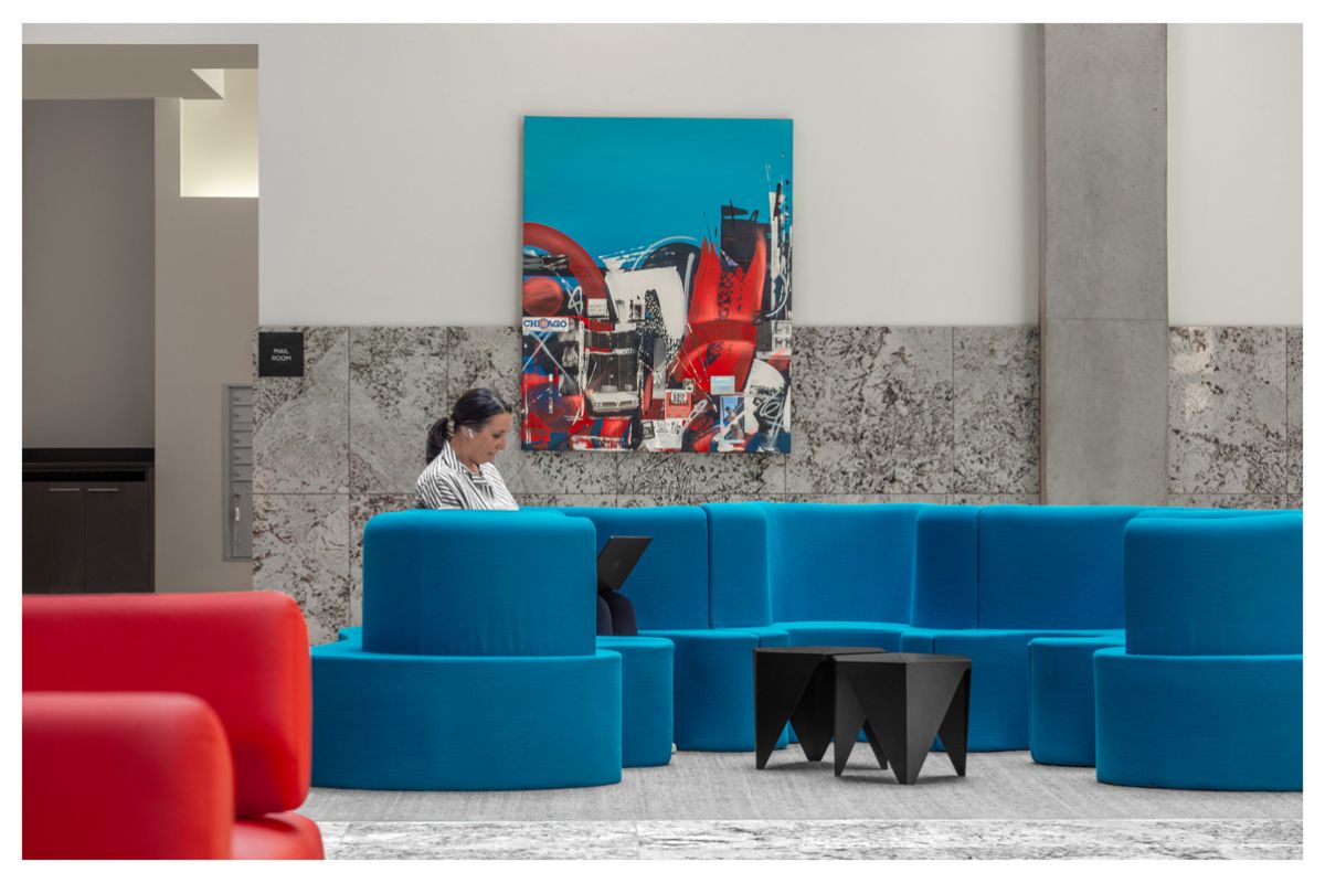 Optima Lakeview® Apartments in Chicago, IL A person works on a laptop while sitting on a blue couch in a modern lobby with colorful artwork on the wall.