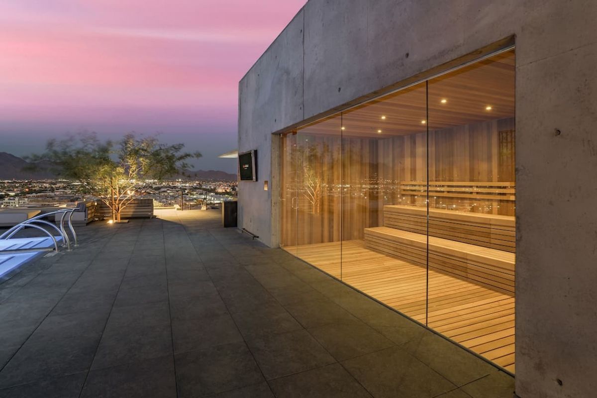 Optima Lakeview® Apartments in Chicago, IL Modern rooftop terrace at sunset with a glass-walled sauna, city lights, and premium well-being amenities by Optima Communities.