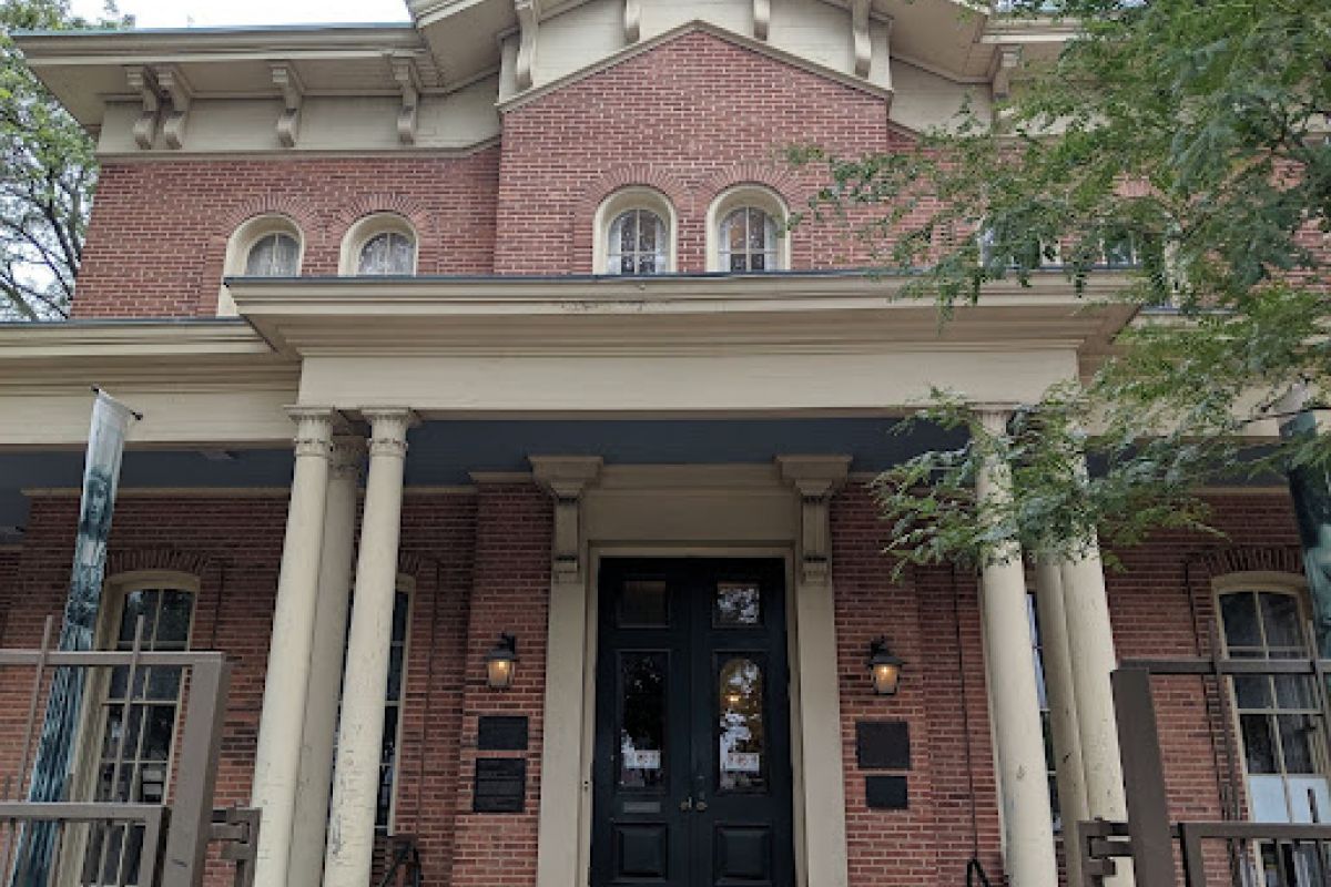 Optima Lakeview® Apartments in Chicago, IL A historic brick building with columns and arched windows, Hull House in Chicago was a center for social reform, partially shaded by trees.