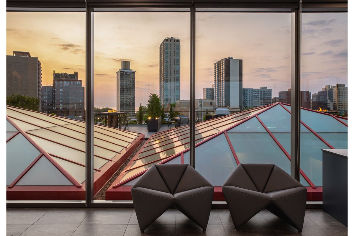 Optima Lakeview® Apartments in Chicago, IL Two modern chairs by large windows, welcoming you home as the city skyline glows with a good night sunset above geometric rooftops.
