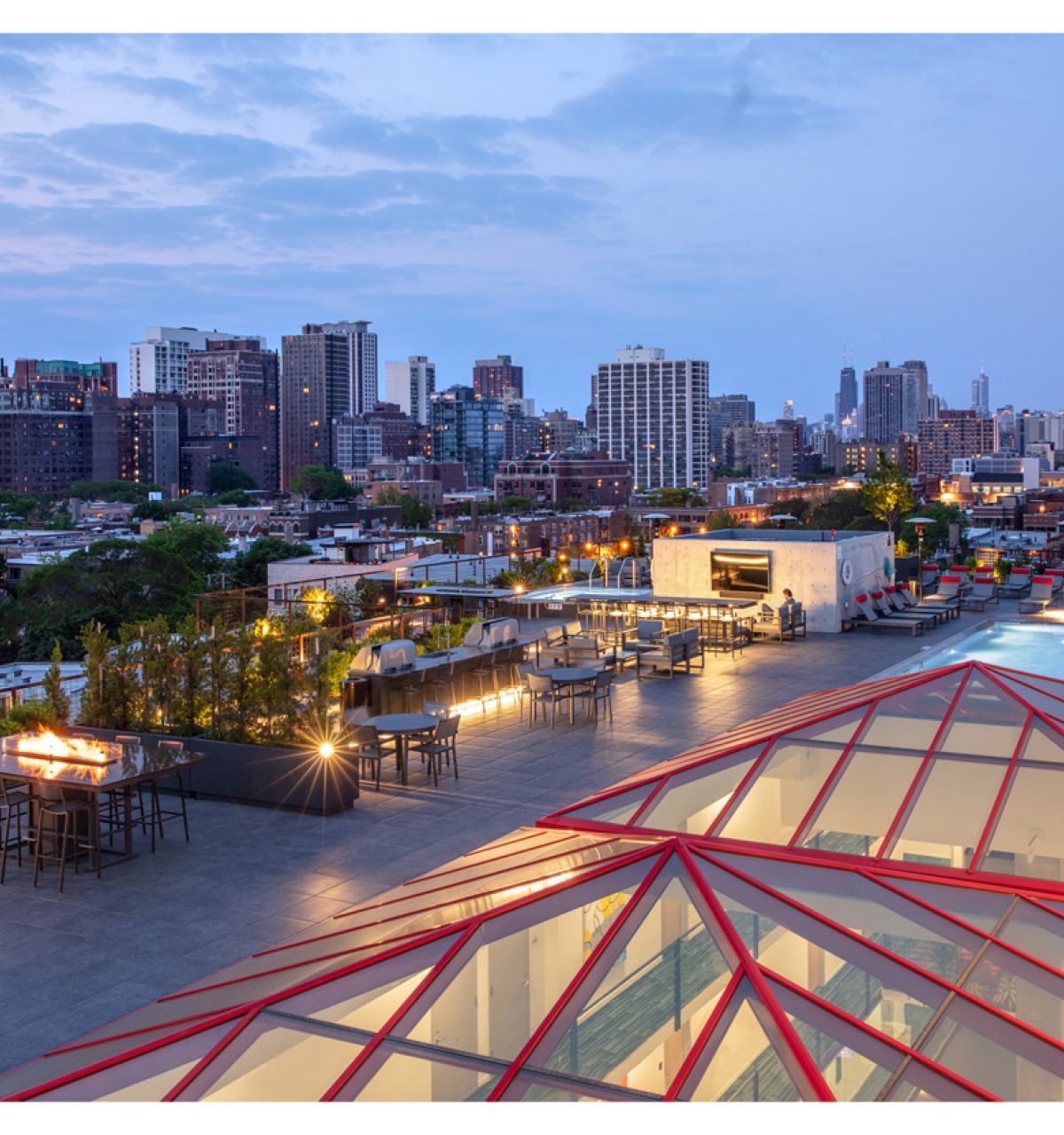 Optima Lakeview® Apartments in Chicago, IL Rooftop patio with seating, fire pits, pool, and city skyline view at sunset—exclusively for Optima Residents to rent and enjoy.