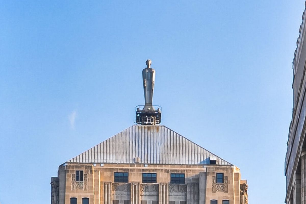 Optima Lakeview® Apartments in Chicago, IL Statue of a man stands atop a tall stone building with a sloped roof in Chicago, framed by two nearby buildings.