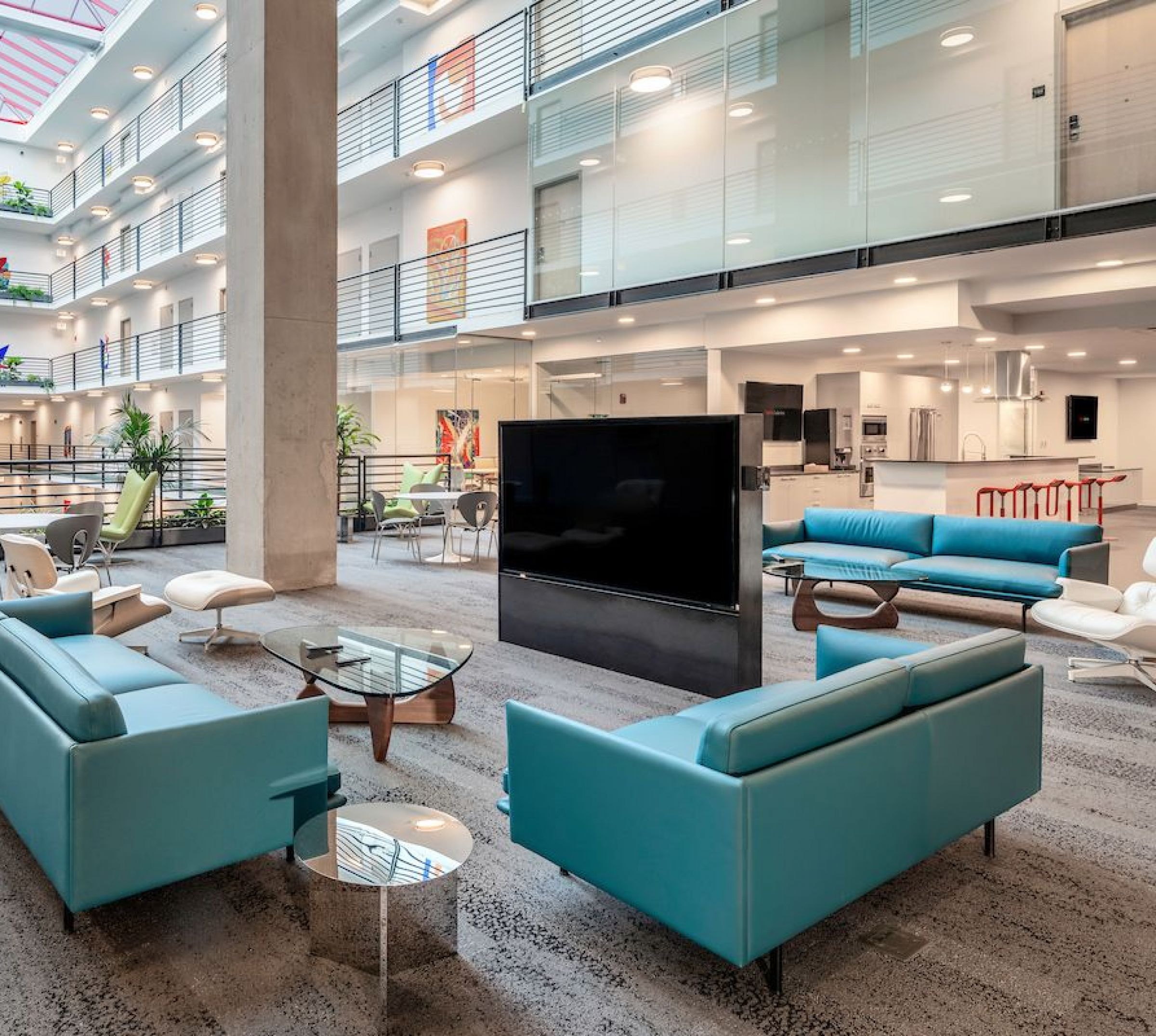 Optima Lakeview® Apartments in Chicago, IL Modern office atrium with blue sofas, lounge chairs, a large TV, and glass railings on upper floors.