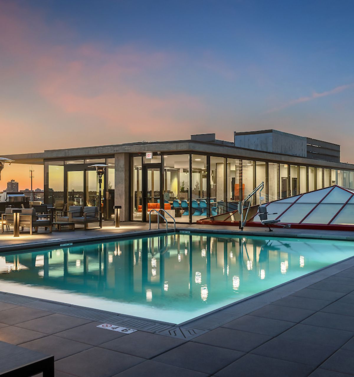 Optima Lakeview® Apartments in Chicago, IL Rooftop pool and lounge area with city skyline views at sunset, alfresco cooking spaces, and modern glass building by Optima Communities.