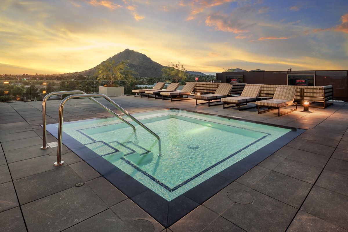 Optima Lakeview® Apartments in Chicago, IL Rooftop hot tub with lounge chairs at sunset—experience scenic living with stunning mountain and city views in the background.