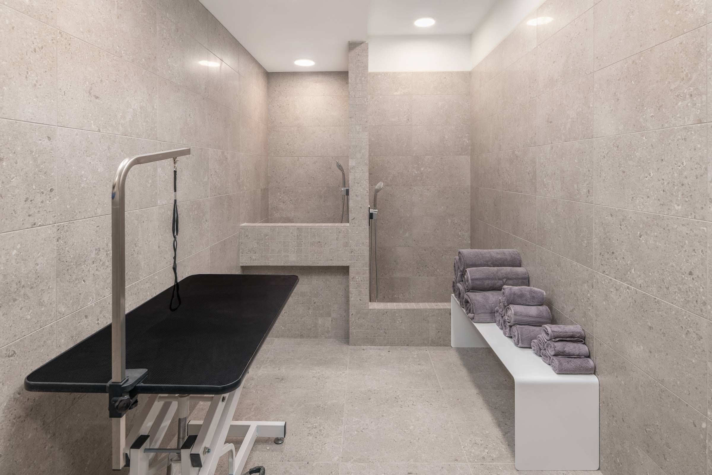 Optima Lakeview® Apartments in Chicago, IL Modern tiled room with a grooming table, stacked towels on a bench, and two walk-in shower stalls.