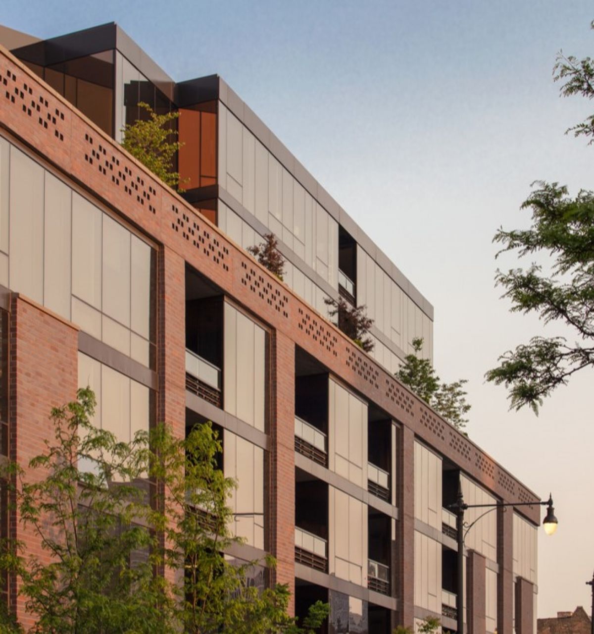 Optima Lakeview® Apartments in Chicago, IL Modern apartment building with large windows, brick facade, and trees in the foreground under a clear sky.