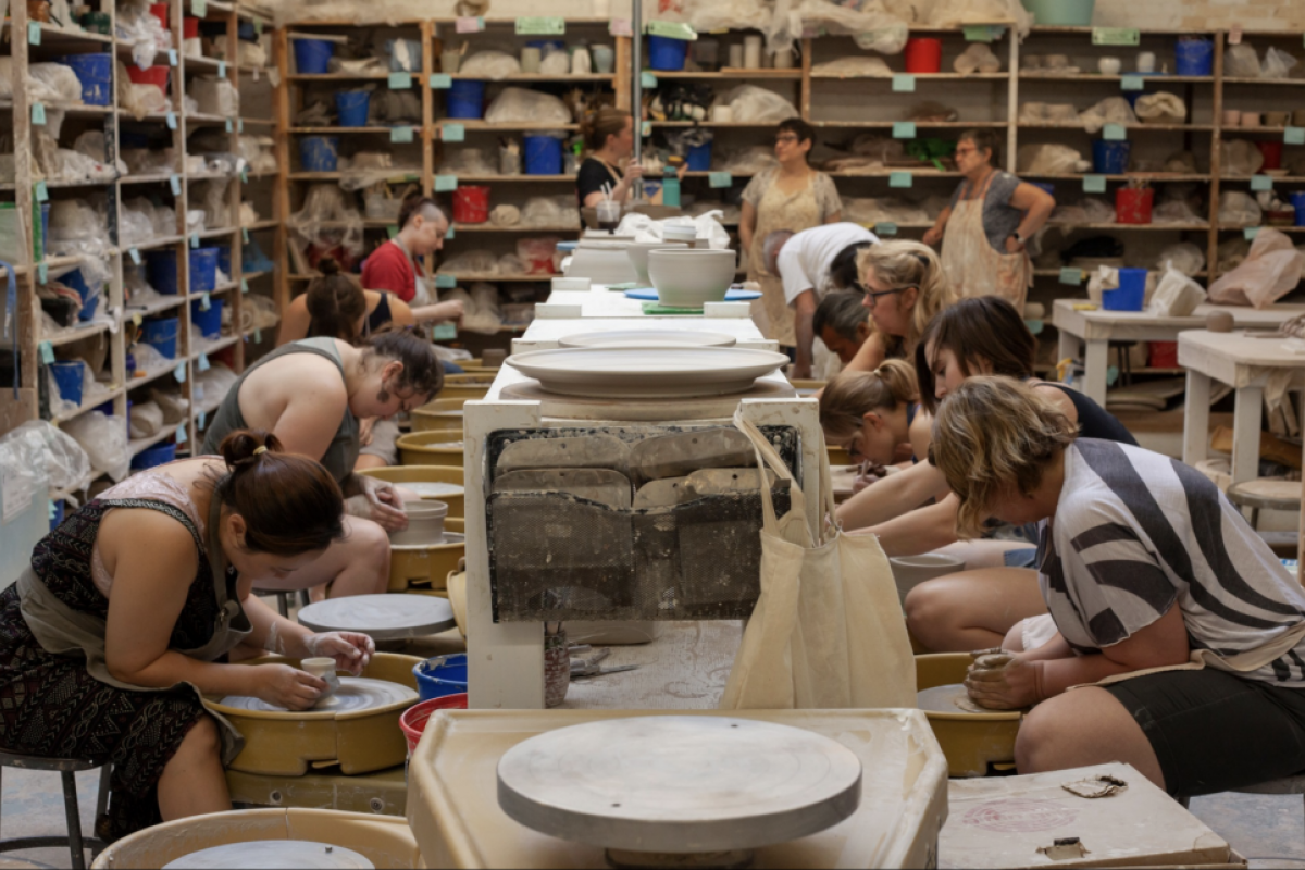 Optima Lakeview® Apartments in Chicago, IL Artists spin clay on pottery wheels at Lillstreet Art Center, surrounded by supplies and bustling with creativity.