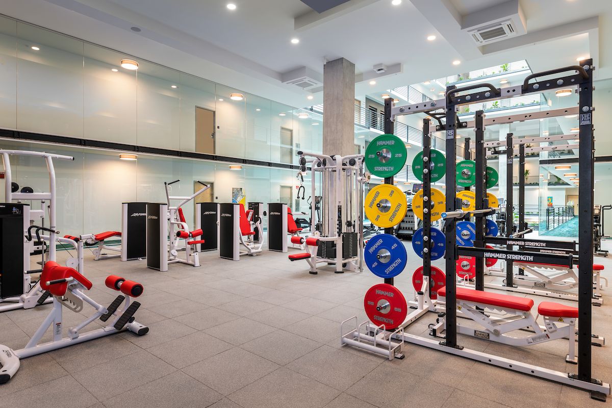 Optima Lakeview® Apartments in Chicago, IL Modern fitness center with weightlifting racks, colorful plates, and various machines to support your daily habit in a spacious room.