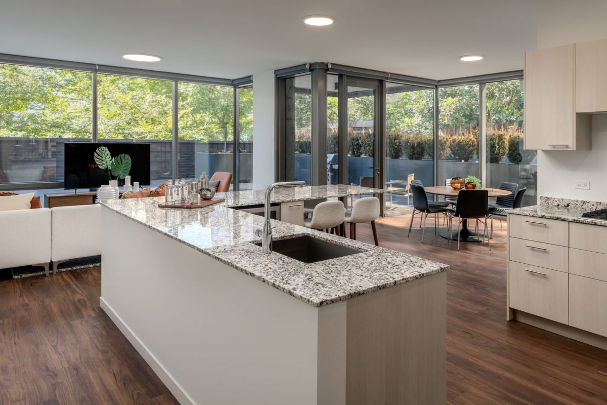 Optima Lakeview® Apartments in Chicago, IL Modern open-concept kitchen and living area features wood floors, Tulip Tables, large windows, and stunning outdoor patio views.