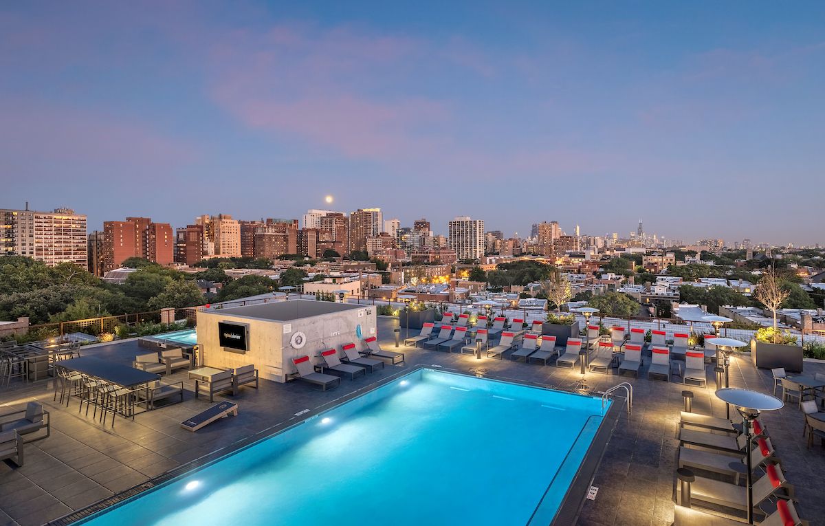 Optima Lakeview® Apartments in Chicago, IL Experience effortless wellness by the rooftop pool as city lights glow and sunset transforms the skyline, lounge chairs inviting pure relaxation.