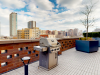 Optima Lakeview® Apartments in Chicago, IL Rooftop patio at Optima with a grill, potted plants, and city buildings—a perfect outdoor space under a partly cloudy sky.