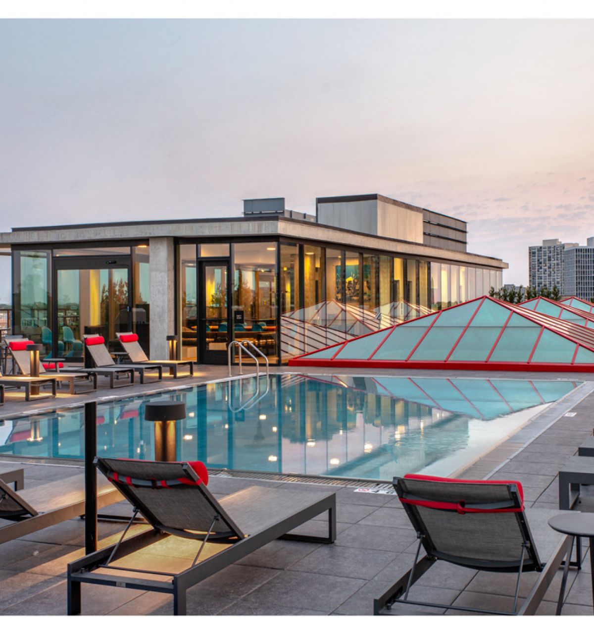 Optima Lakeview® Apartments in Chicago, IL Enjoy stunning evenings on the Sky Deck, featuring a rooftop pool, lounge chairs, red accents, and city views at sunset.