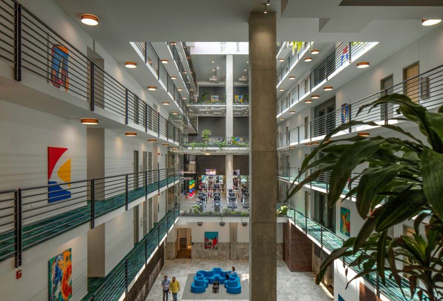 Optima Lakeview® Apartments in Chicago, IL Modern indoor atrium with balconies, artwork on walls, blue seating, and plants; people walking below.